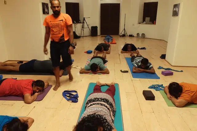 Abhilash teaching an indoor class, students resting forward on their mats.