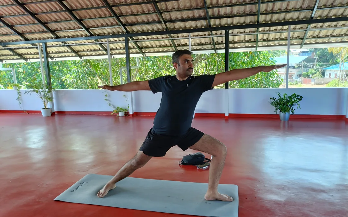 A student holding warrior two on the mat in the open-sided shala.